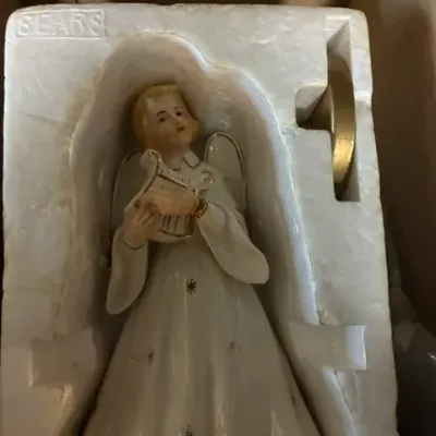 Vintage Sears porcelain angel tree topper playing a harp, nestled in its original styrofoam packaging.