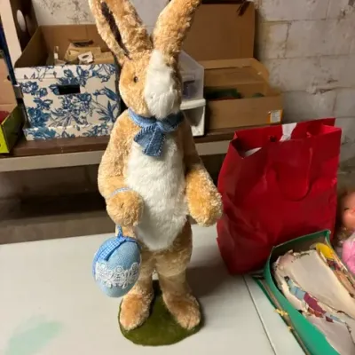 Vintage standing Easter bunny decoration, featuring plush tan and white fur, a blue neck bow, and holding a matching blue Easter egg.