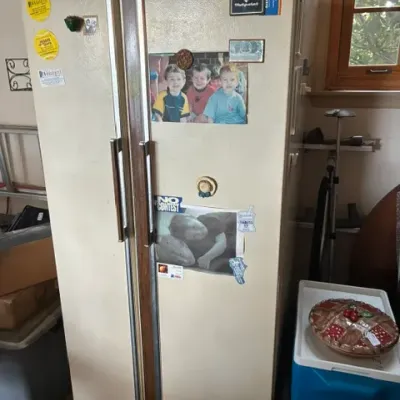 Vintage Hotpoint side-by-side refrigerator in almond finish with faux wood grain handles, showing some wear and age.