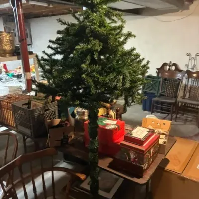 Artificial Christmas tree with a slender trunk design, displayed alongside various holiday storage boxes and basement furniture.
