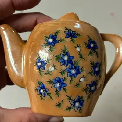 Vintage miniature ceramic teapot featuring a peach lusterware glaze and hand-painted blue floral details.