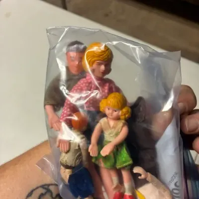 Vintage plastic and cloth family doll figures, including parents and children, packaged together in a clear plastic bag.