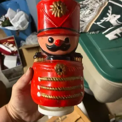 Vintage plastic toy soldier bank in bright red and gold, featuring a hand-painted mustache and uniform details.