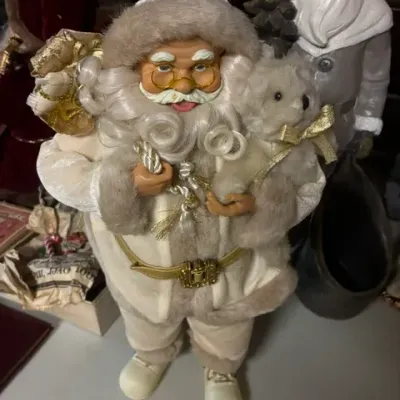 Vintage Santa Claus figurine dressed in a white and gold suit, holding a small teddy bear and a sack of toys.