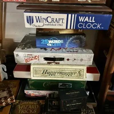 Stack of vintage and modern board games, including Monopoly M&M's Collector's Edition, Risk Legacy, Huggermugger, and...