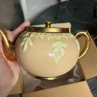 Vintage Sadler-style teapot featuring a peach-colored body with cream-colored relief leaf details and gold-gilded handle, spout, and lid.