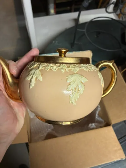 Vintage Sadler-style teapot featuring a peach-colored body with cream-colored relief leaf details and gold-gilded handle, spout, and lid.