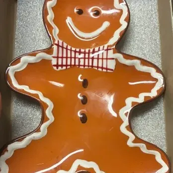 Gingerbread man ceramic spoon rest or small dish, featuring a glossy finish with painted white icing details and a red plaid bow tie.