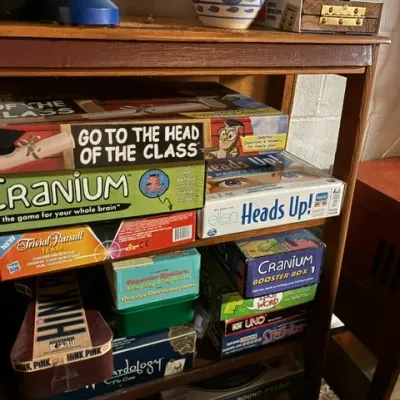 A collection of vintage and modern board games, including Cranium, Go to the Head of the Class, and Heads Up!, arranged on a wooden...