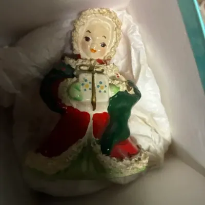 Vintage mid-century ceramic Christmas figurine depicting a girl in a winter coat holding a gift, nestled in tissue paper inside a box.
