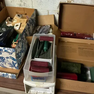 Assortment of unused candles in various colors and sizes, organized in cardboard boxes and a plastic storage drawer.