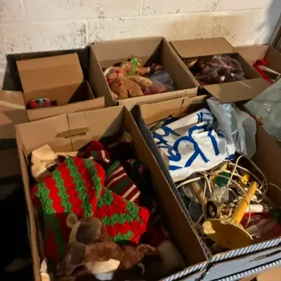 Assorted boxes of vintage Christmas decorations, including crocheted stockings, plush toys, and holiday lighting.