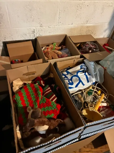 Assorted boxes of vintage Christmas decorations, including crocheted stockings, plush toys, and holiday lighting.