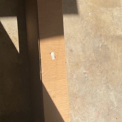 Long, rectangular cardboard shipping box, taped shut and resting on a concrete floor.