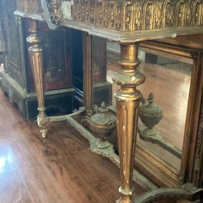Antique Neoclassical style giltwood console table with a marble top, fluted legs, and a mirrored back panel, showing some wear and...
