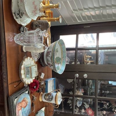Assortment of vintage collectibles displayed on a wooden table, including a large Chinese Famille Rose porcelain bowl, decorative plates,...