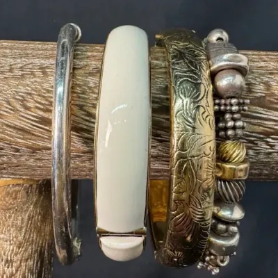 Assortment of vintage bracelets displayed on a wooden stand, including a silver-tone bangle, a cream enamel hinged bangle, an ornate...