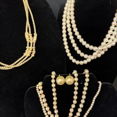 Assortment of vintage multi-strand faux pearl necklaces and a pair of matching clip-on earrings displayed on black velvet busts.