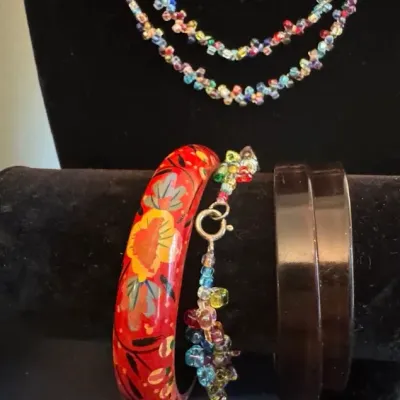 Assorted vintage jewelry including a hand-painted red floral wooden bangle, a dark brown plastic bangle, and colorful beaded necklaces...