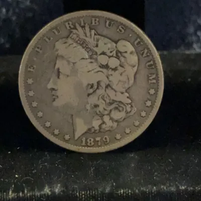 An 1879 Morgan silver dollar showing the obverse side with Liberty's profile, displaying moderate wear and a natural patina.
