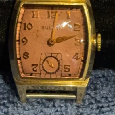 Vintage Bulova gold-tone tank watch featuring a salmon-colored dial with Arabic numerals and a sub-second dial, showing some wear and...