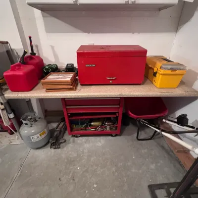 Stack-On red metal tool chest and rolling cabinet set, shown alongside a yellow plastic utility box, gas cans, and a propane tank in a...