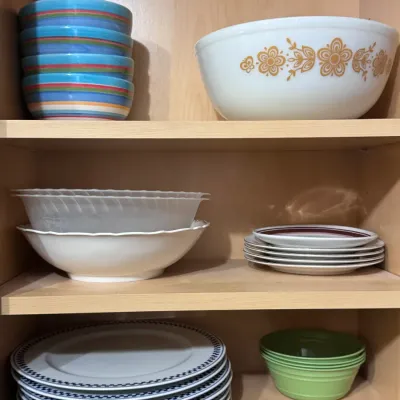 Vintage Pyrex Butterfly Gold mixing bowl, made in the USA, displayed alongside a collection of colorful ceramic bowls, patterned dinner...