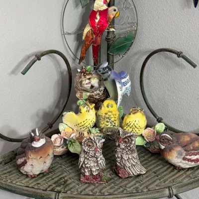 Collection of vintage ceramic bird figurines, including a blue jay at a nest, yellow canaries, owls, and quail, displayed on a metal...