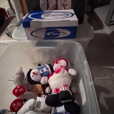 Collection of plush snowman Christmas decorations in a clear plastic storage bin, shown alongside a vintage Turntec shoebox and an...