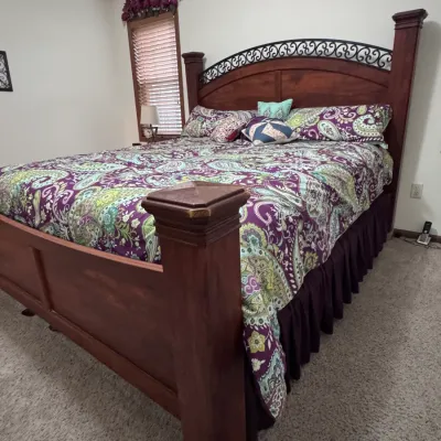 Traditional wooden king-size bed frame featuring a high arched headboard with decorative black wrought iron scrollwork, thick square...