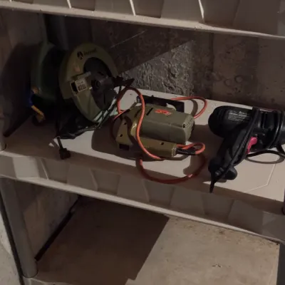 Vintage Rockwell circular saw and jigsaw, alongside a modern black power drill, displayed on a plastic utility shelf.