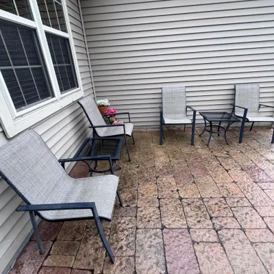 Modern outdoor patio set featuring four grey mesh sling armchairs with dark metal frames and two matching glass-top side tables, arranged...