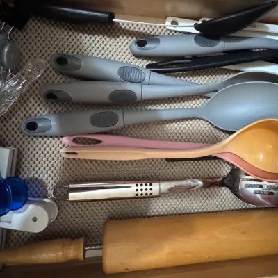 Assorted kitchen utensils in a drawer organizer, including a wooden rolling pin, a stainless steel slotted spoon, colorful plastic...