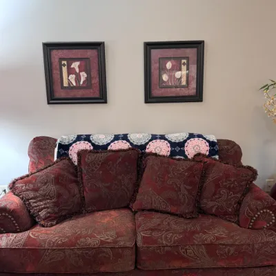 Traditional burgundy paisley upholstered loveseat featuring rolled arms with brass nailhead trim, bun feet, and four matching fringed...