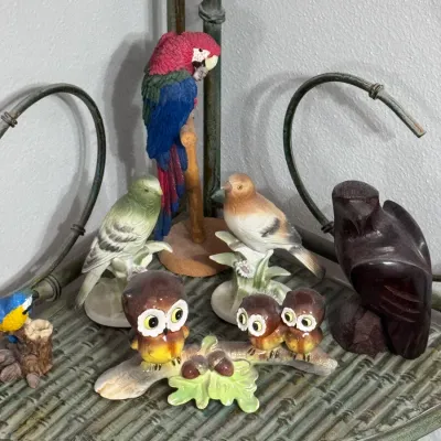 Collection of vintage bird figurines, including a hand-painted porcelain owl family on a branch, a colorful resin macaw on a perch, and a...
