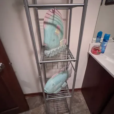 Four-tier silver metal wire shelving unit, ideal for bathroom storage, displaying two pastel-painted carved wooden fish sculptures.