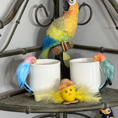 Tropical parrot-themed decor collection featuring a hand-carved wooden parrot figurine, two white ceramic mugs with colorful...