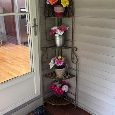 Four-tier metal corner baker's rack in a bronze finish, featuring scrollwork details and mesh shelves, styled with potted artificial...