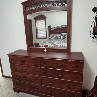 Traditional cherry-finished wooden dresser with matching landscape mirror, featuring scrollwork metal accents, multiple drawers with...