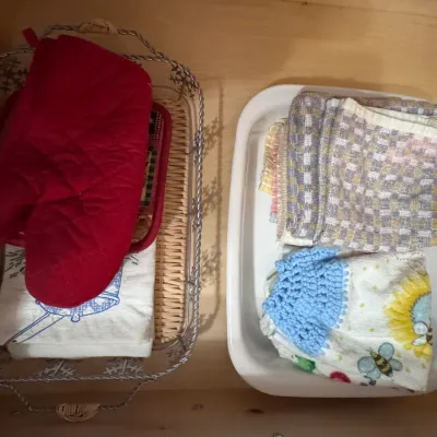 Assorted kitchen linens, including a red quilted oven mitt, patterned dish towels, and a crocheted hand towel, organized inside a...