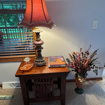 Mission-style oak end table featuring a slatted lower shelf, paired with an ornate traditional table lamp with a scalloped fabric shade.