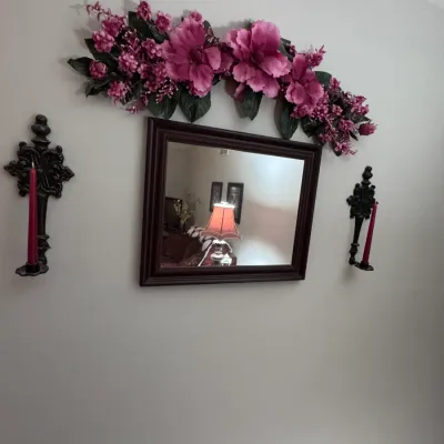 Traditional dark wood framed wall mirror, flanked by a pair of black cast iron gothic-style candle sconces with red taper candles, topped...