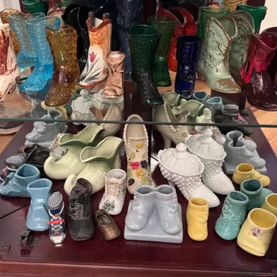 Collection of vintage ceramic and glass shoe figurines, featuring Fenton hobnail boots, Victorian-style slippers, and colorful cowboy...
