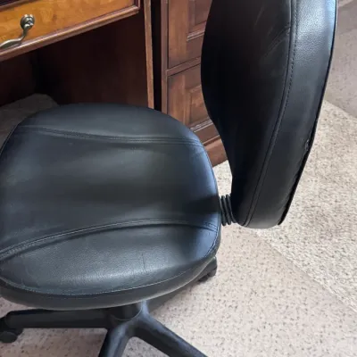 Black faux leather rolling office chair with an adjustable backrest and a five-star caster base, shown in gently used condition next to a...