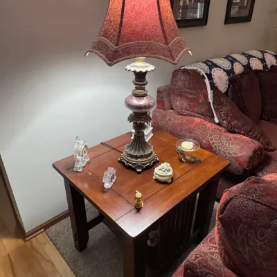 Traditional wooden end table featuring a mission-style slatted base, topped with an ornate vintage-style table lamp with a red fabric...