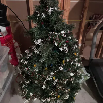 Small pre-lit artificial Christmas tree decorated with white snowflake ornaments and tinsel garland, standing on a metal base.