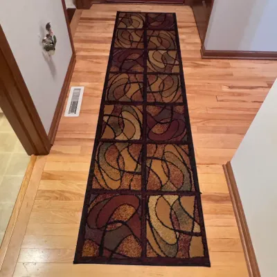 Contemporary geometric hallway runner rug featuring a grid pattern with abstract swirl designs in warm earth tones of brown, gold, and...