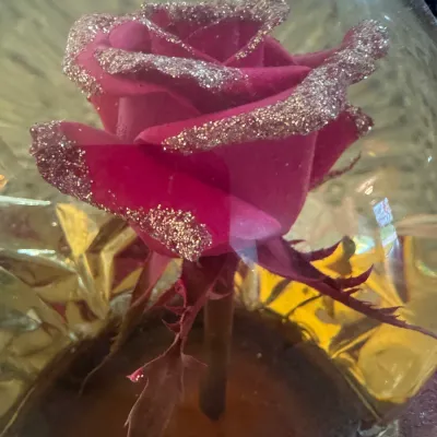 Decorative pink rose with gold glitter-trimmed petals, encased in a clear glass dome with a gold foil background, suitable for home decor...