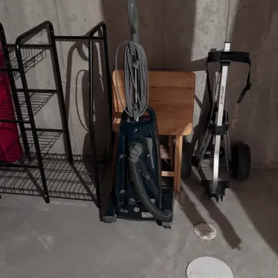Hoover upright vacuum cleaner, a Diplomat pull-behind golf cart, a wooden folding table, and a black wire shelving unit, all showing...