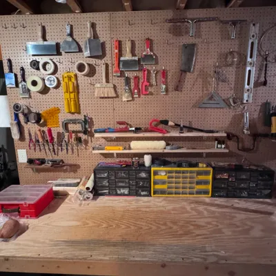Workshop workbench and pegboard organizer featuring an assortment of hand tools, including drywall taping knives, scrapers, paint...